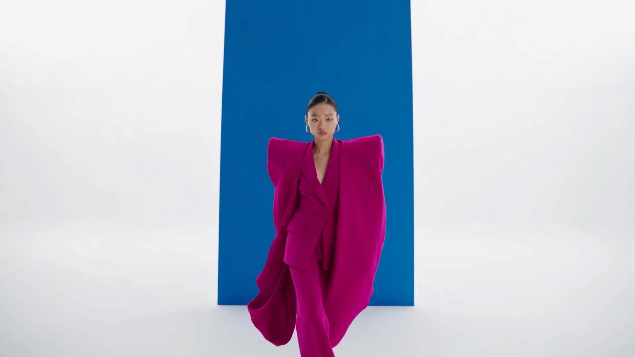 Una mujer con un atuendo magenta vaporoso sobre un fondo llamativo azul y blanco