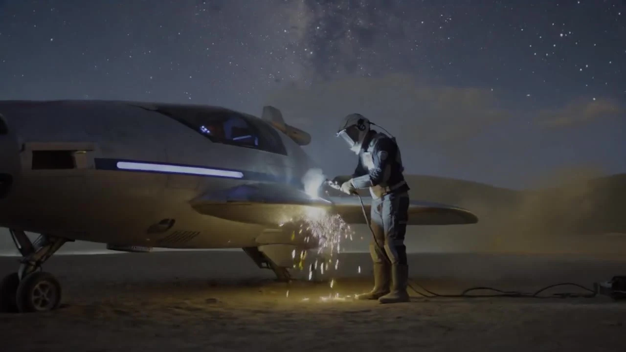 A helmeted worker welding beside a futuristic vehicle under a starry sky
